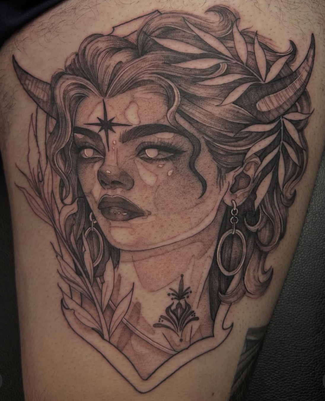Fine line tattoo of a horned woman with flowing hair, and decorative leaves around her head and neck.