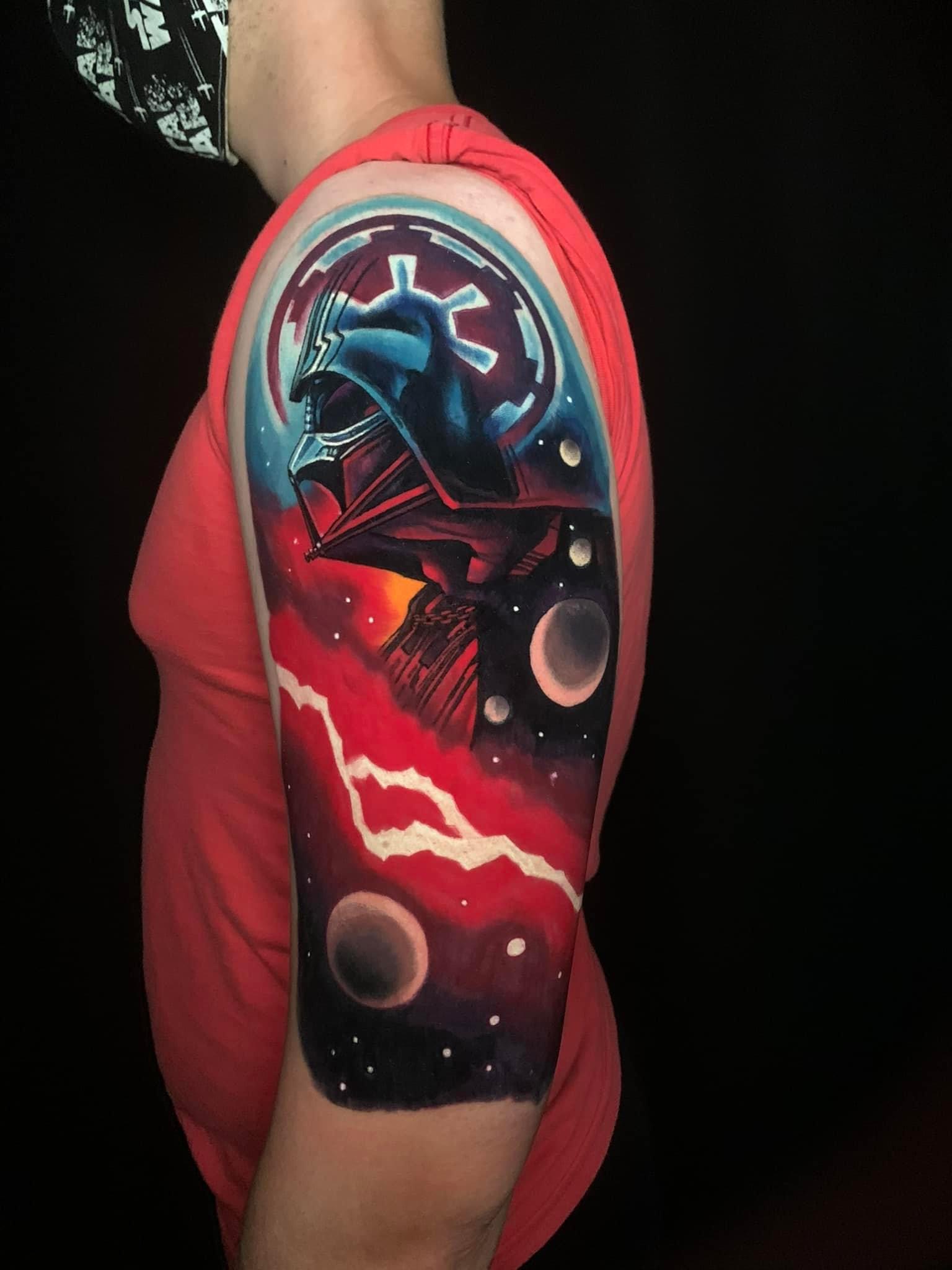 Tattoo of Darth Vader’s helmet with Galactic Empire emblem, planets, and space scene on upper arm.