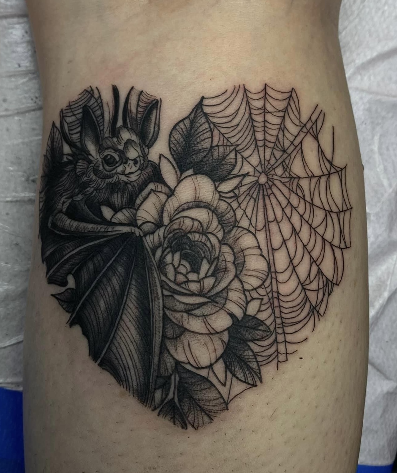 Fine line tattoo of a bat with detailed wings resting on a large rose with leaves and a spider web in the background.