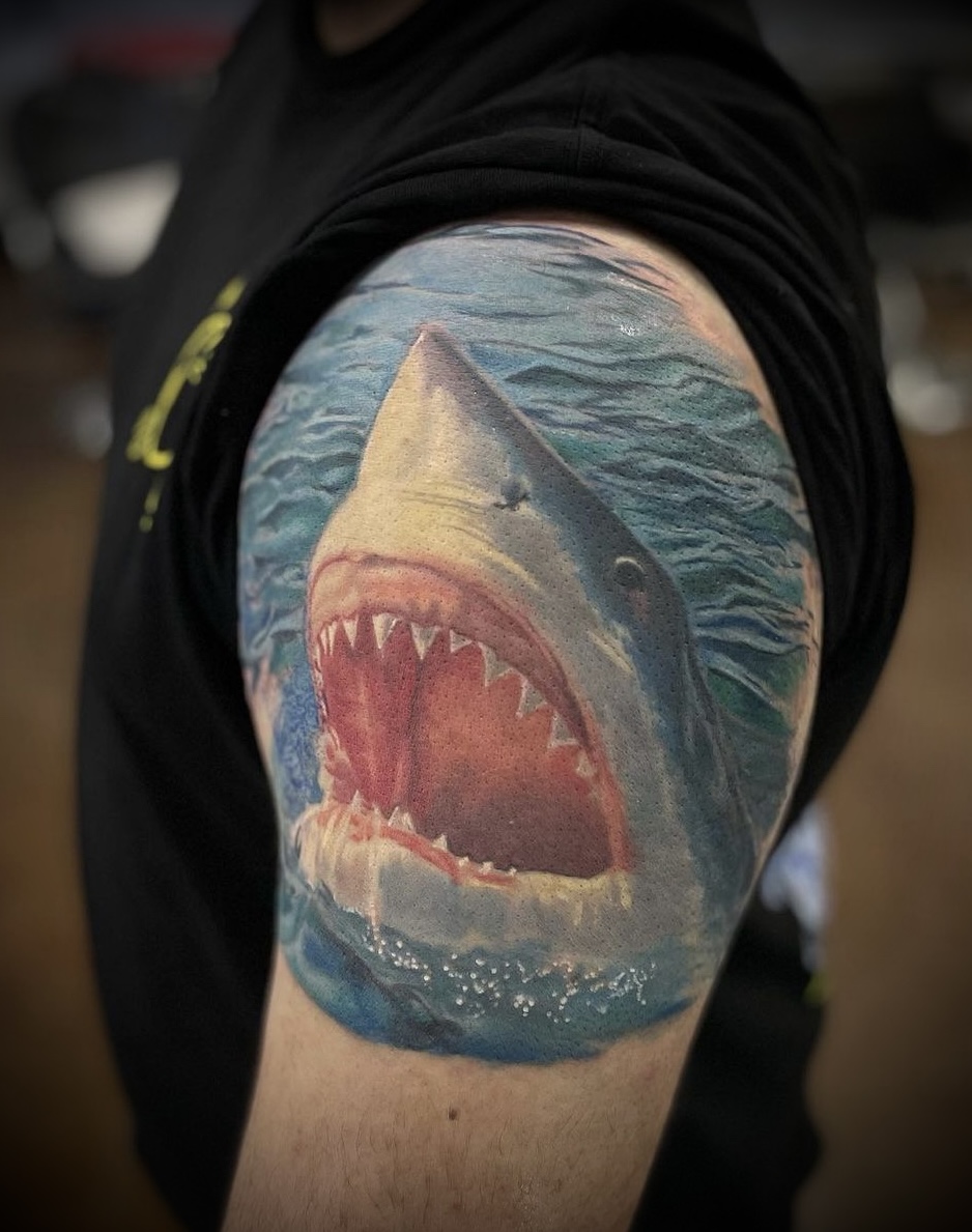 Color realism tattoo of a great white shark Jaws emerging from water.