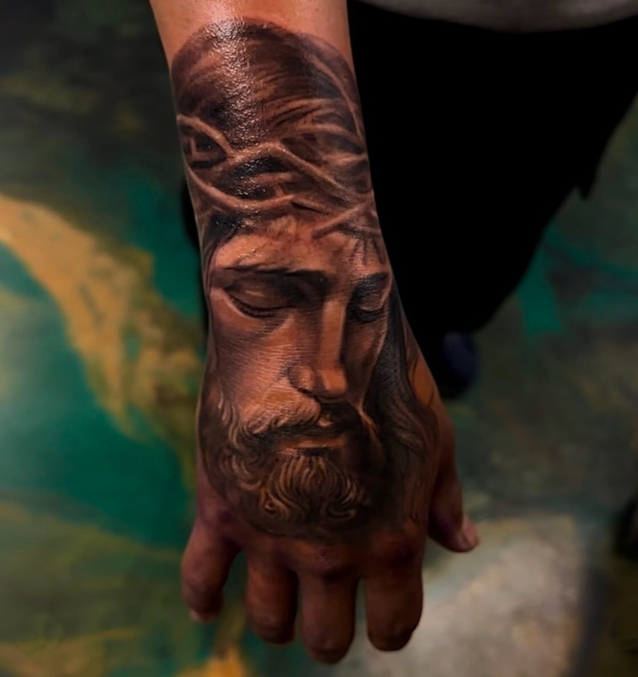 Realistic tattoo of Jesus Christ with crown of thorns on the back of a person's hand.