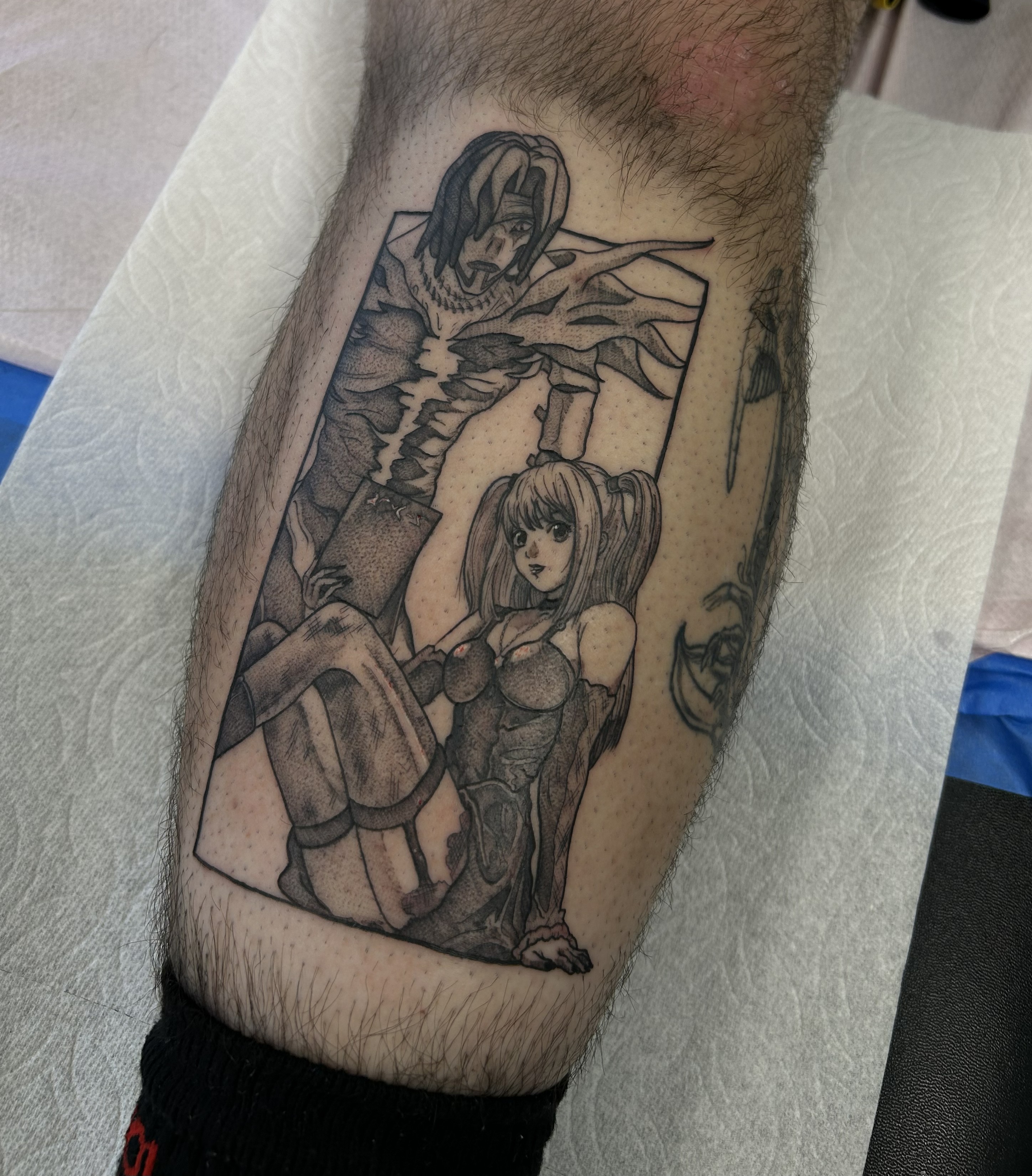 Fine line tattoo on a leg depicting a anime man with long hair and a flowing cloak behind a seated woman with pigtails.