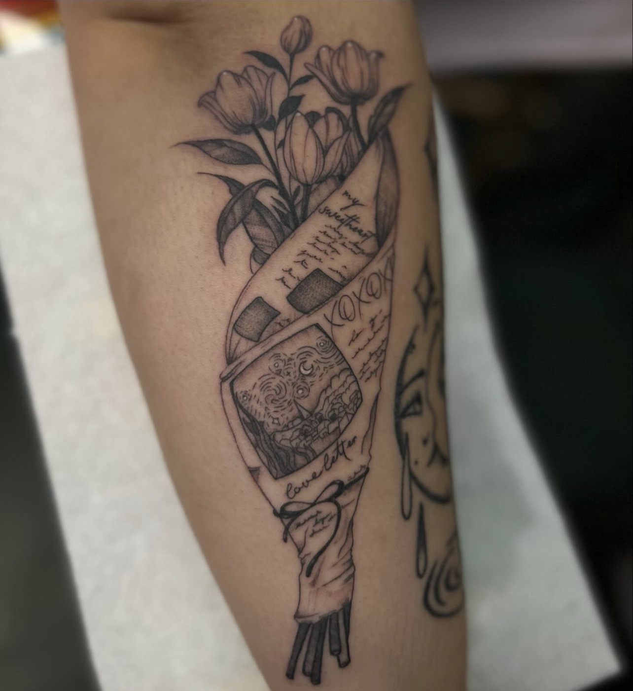 Fine line tattoo of a bouquet of tulips wrapped in paper featuring a love letter.