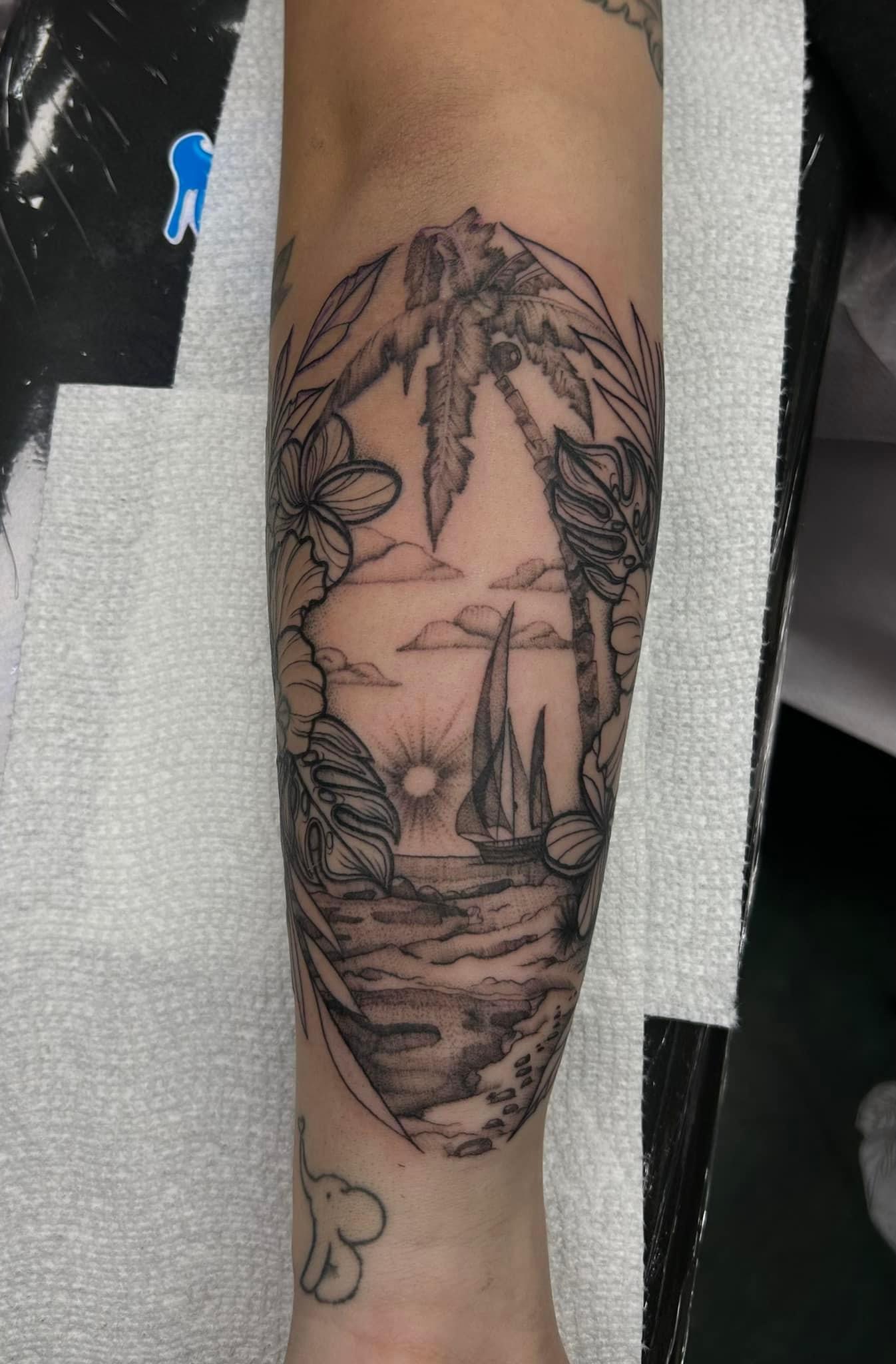 Forearm tattoo of a tropical seascape with palm trees, sailboats, sun, clouds, flowers, and leaves.