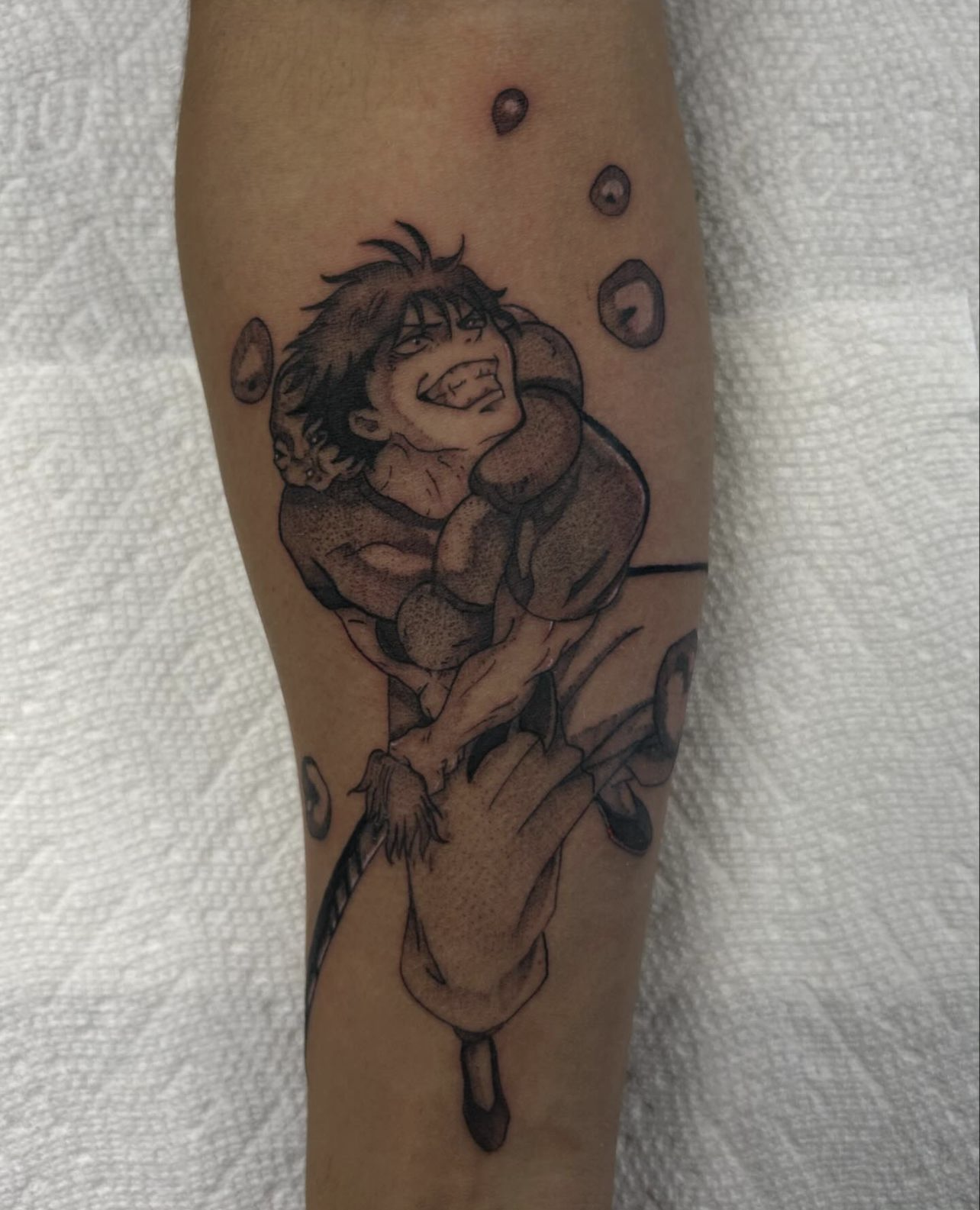 Fine line tattoo of a grimacing muscular anime character with wild hair holding a large weapon on forearm.
