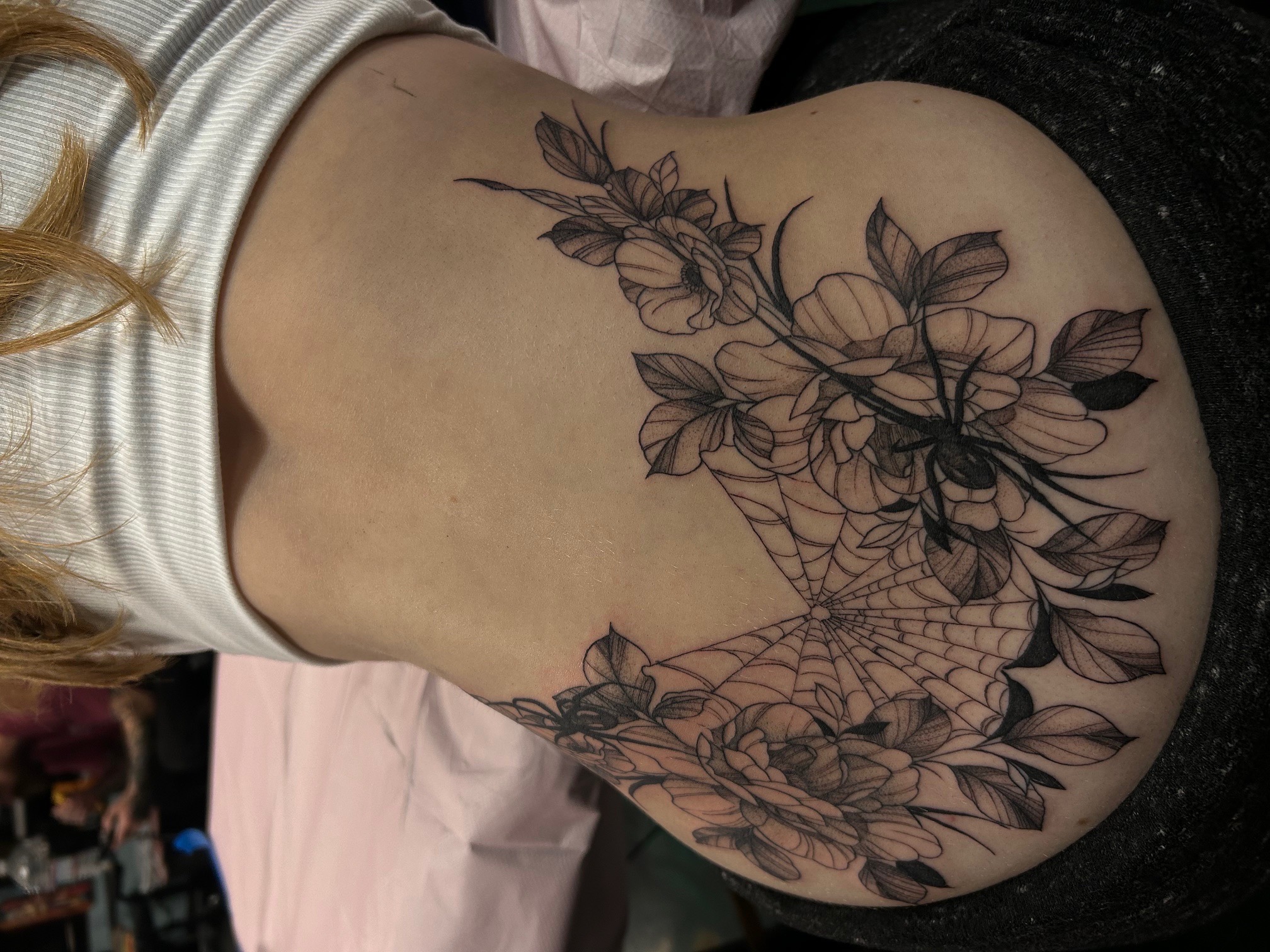 Tattoo of a spider web with a large spider in the center, surrounded by detailed flowers.