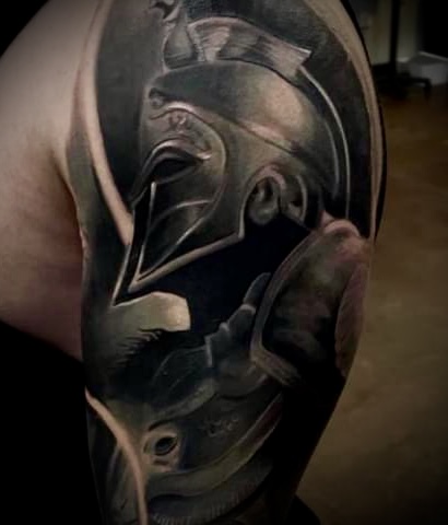 Black and gray tattoo of a Spartan warrior helmet on an upper arm.