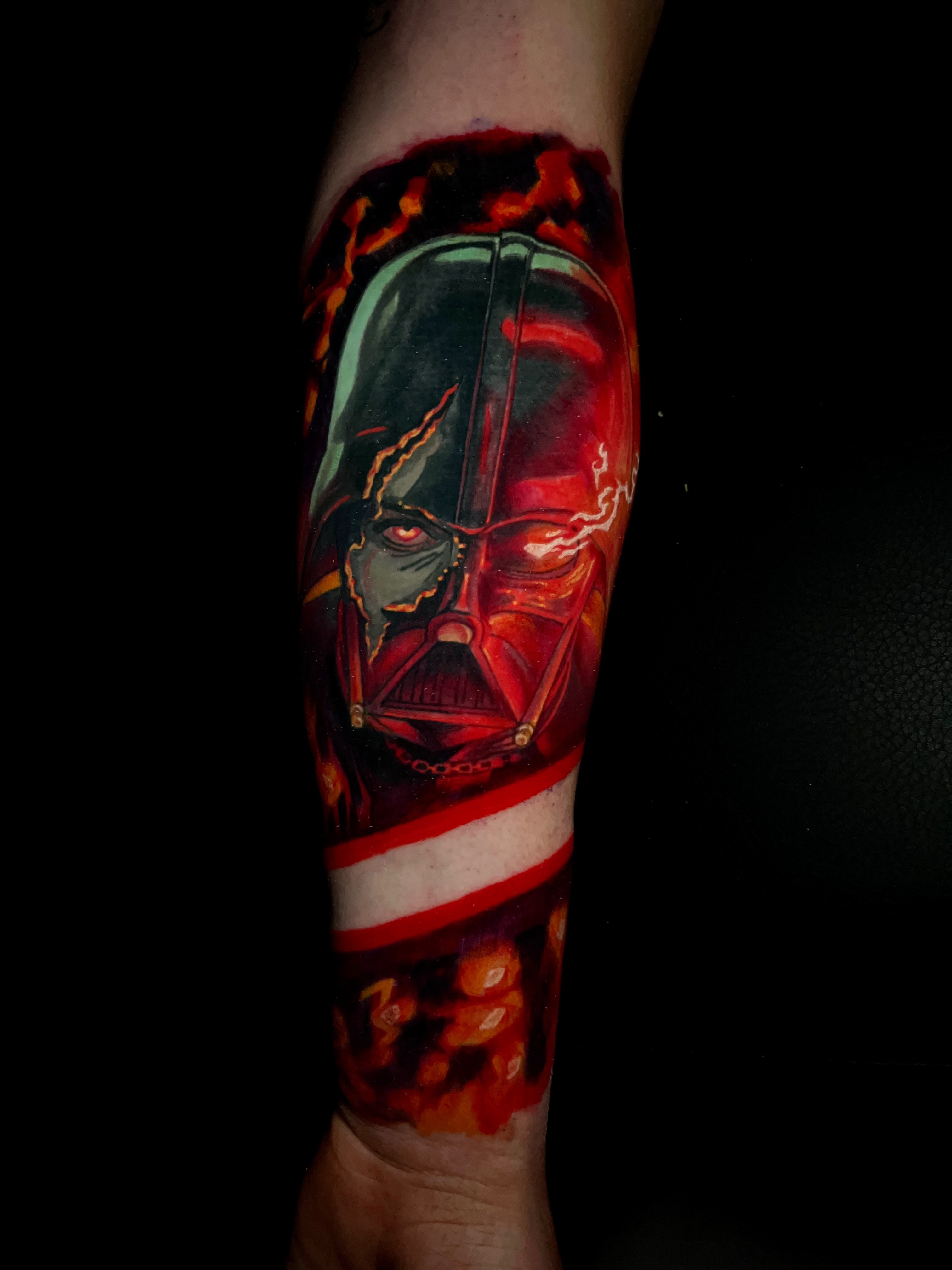 Forearm tattoo of a fiery and damaged Darth Vader helmet with glowing red eyes and dark background.