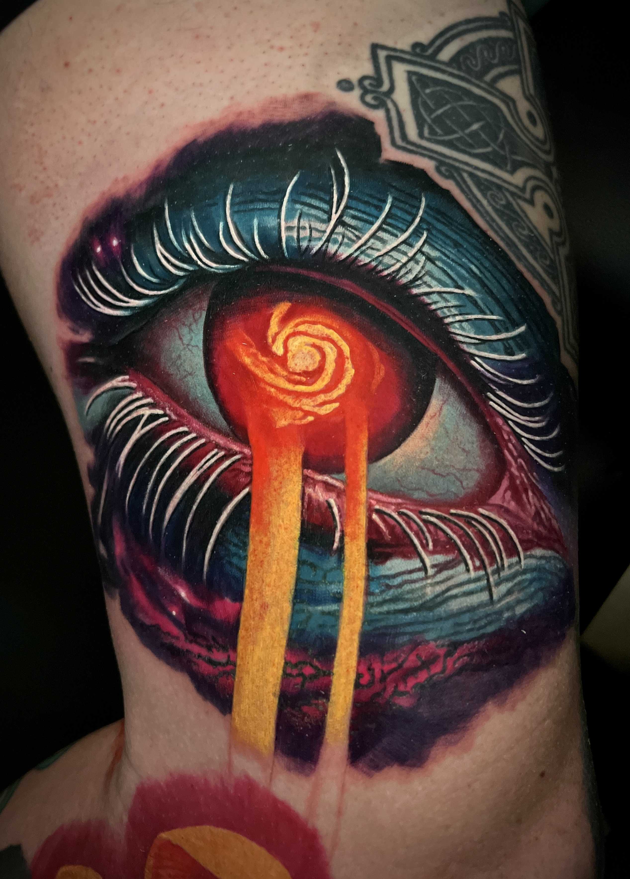Colorful tattoo of a realistic eye with white eyelashes and a spiral iris, with bright orange tears flowing down.