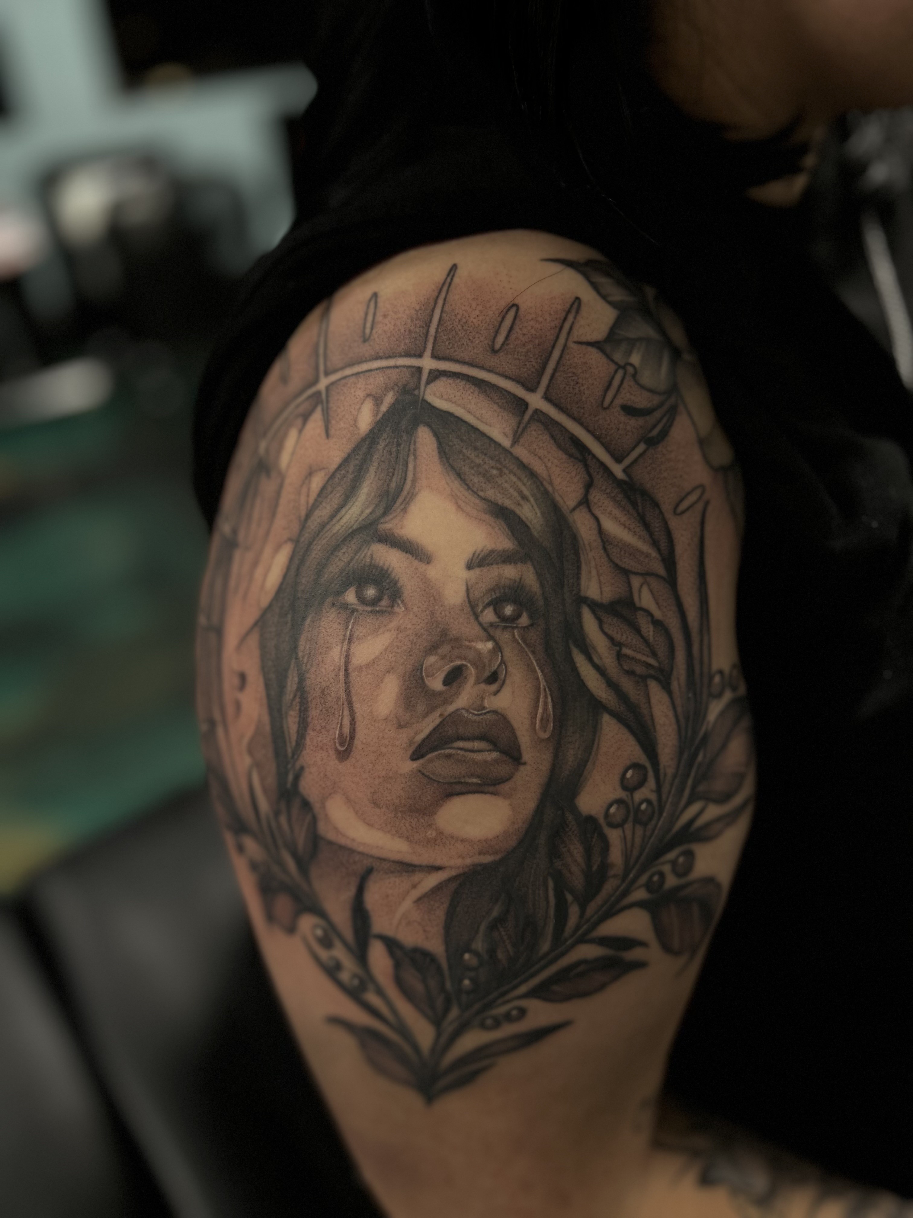 Fine line black and gray tattoo of a crying woman's face surrounded by leaves