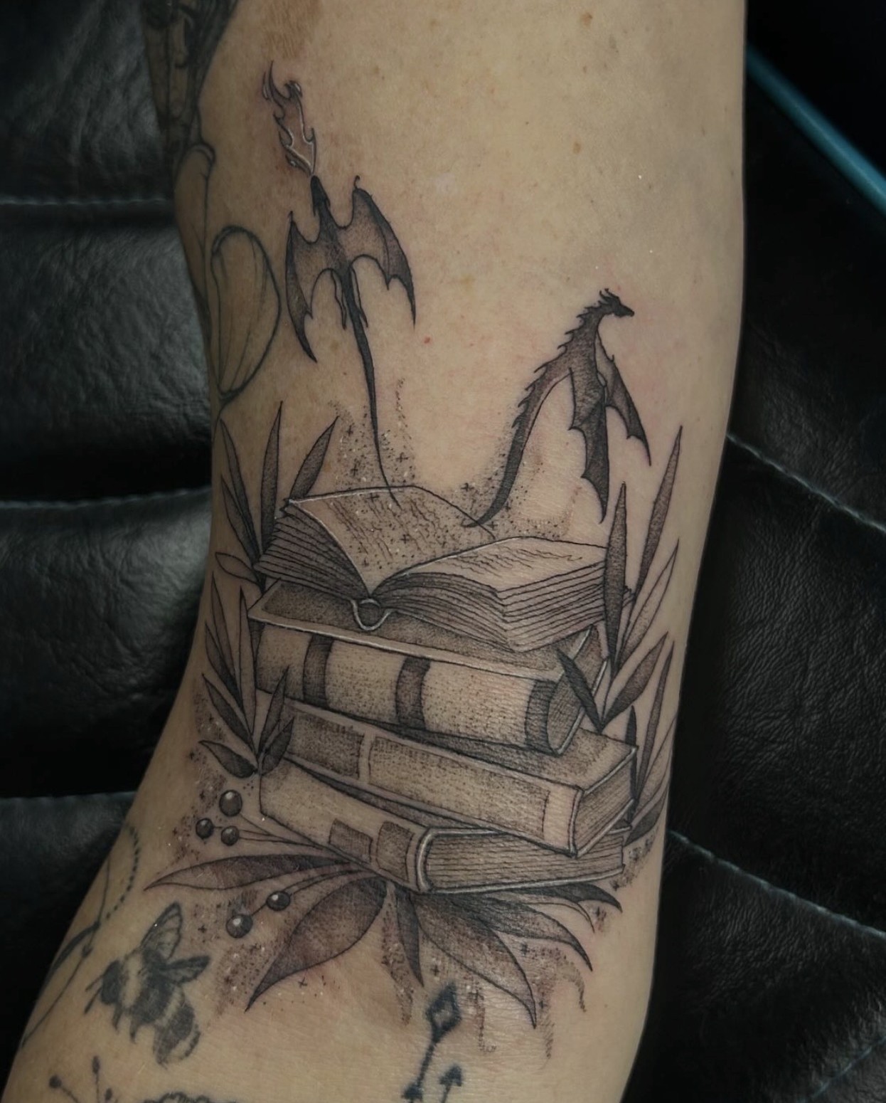 Fourth Wing fine line black and gray tattoo of a stack of books with leaves and dragons