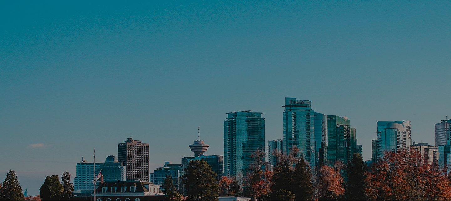 Downtown city skyline with modern high-rise buildings and trees with autumn foliage under a clear blue sky.