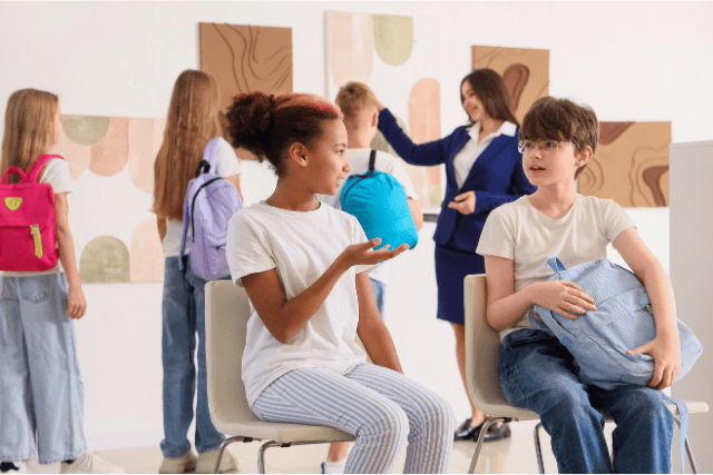 Dos adolescentes sentados conversando con grupo de jóvenes en el fondo observando un cuadro