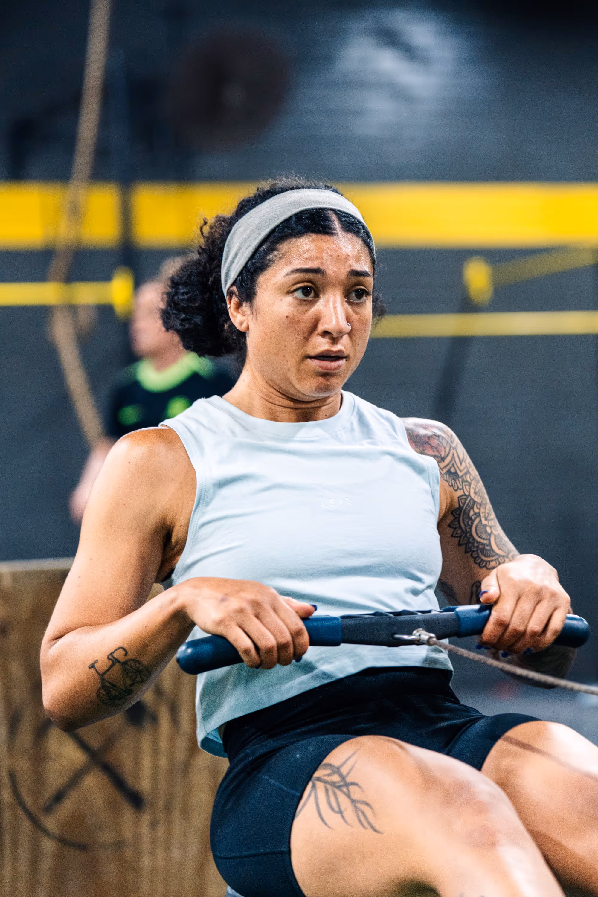 Woman with tattoos and a headband using a rowing machine in a gym.