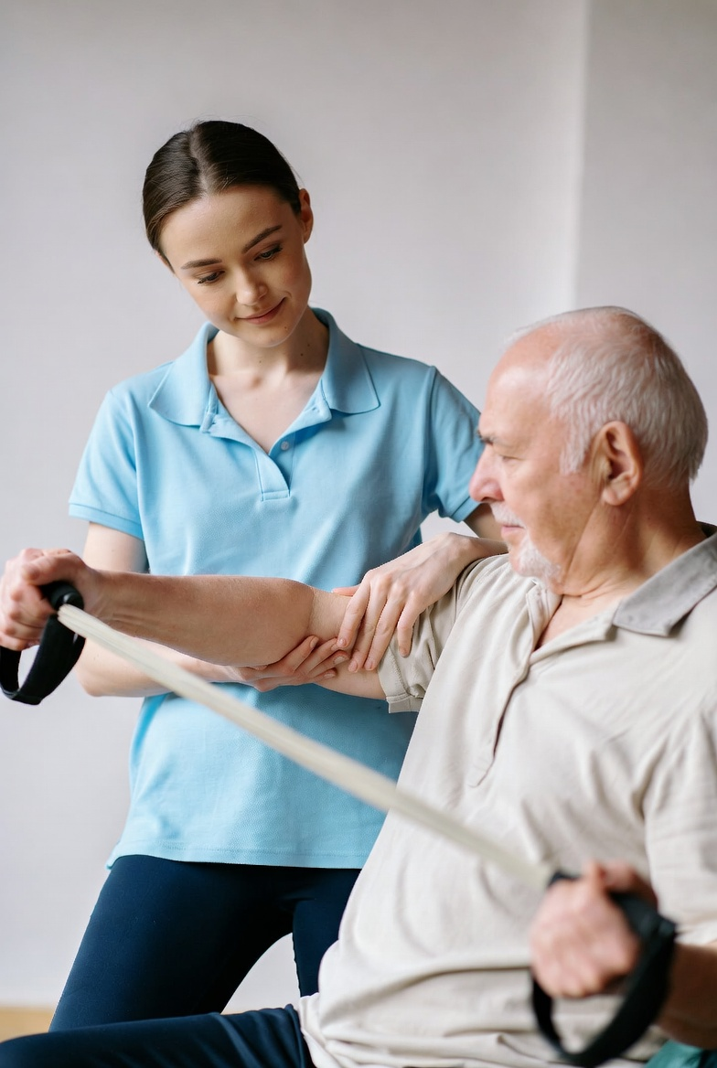 Physical therapist assisting an elderly man with arm exercise using a resistance band.
