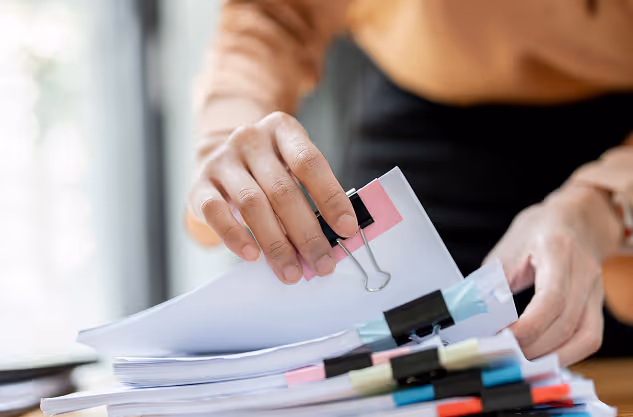Person organizing thick stacks of papers with binder clips on a wooden desk.