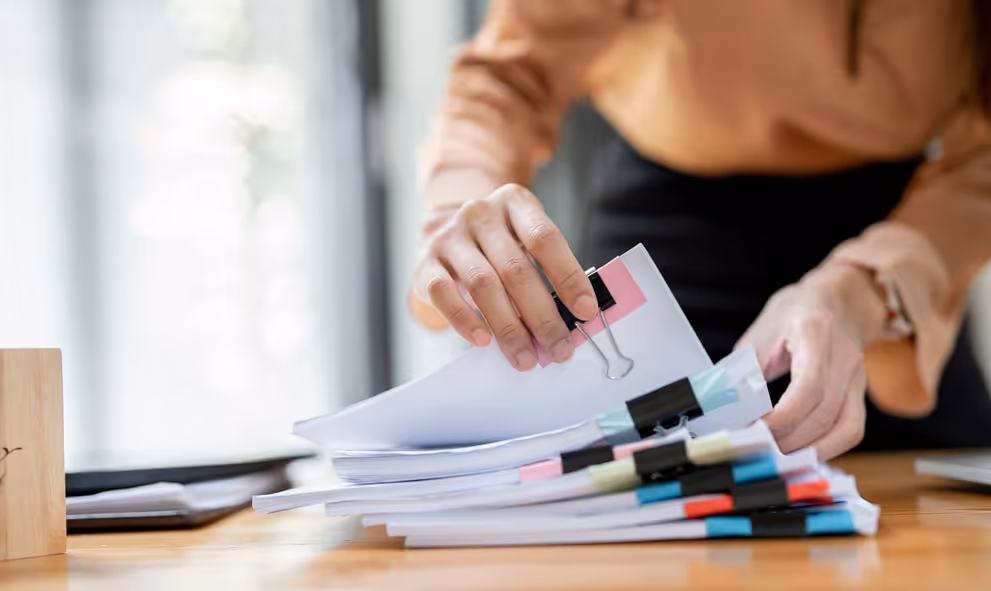Person organizing multiple stacks of documents clipped with binder clips on a wooden table.