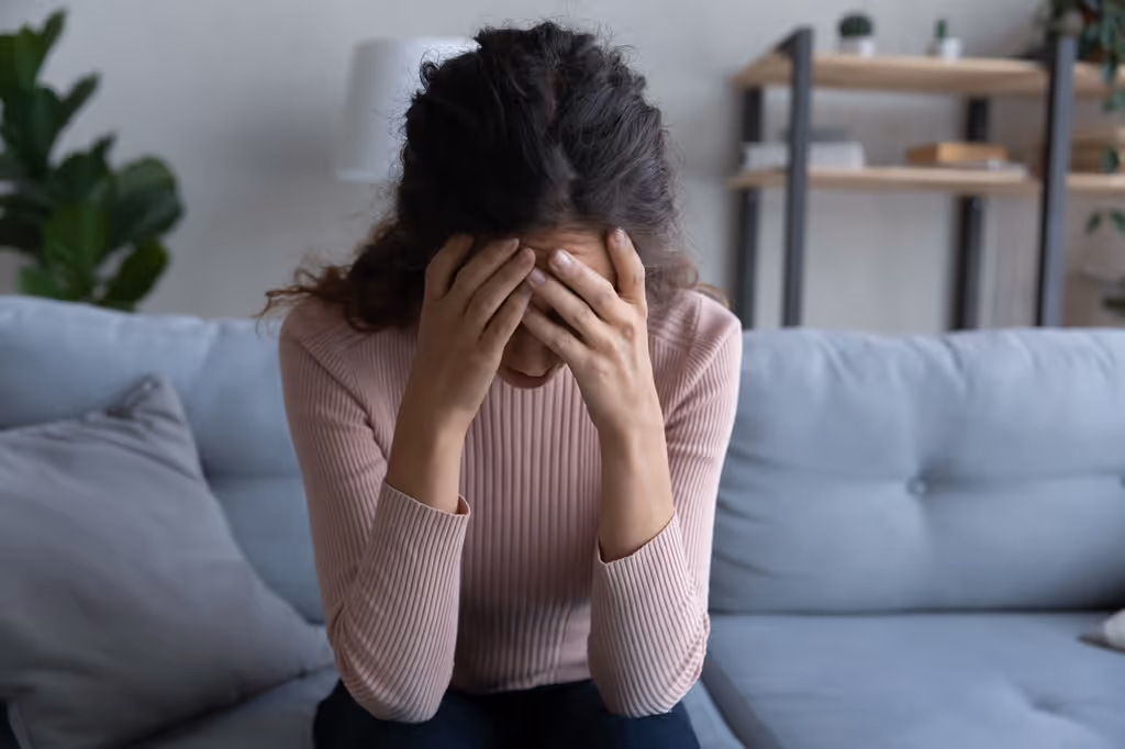 Woman sitting on a couch with her head in her hands, appearing stressed or overwhelmed.