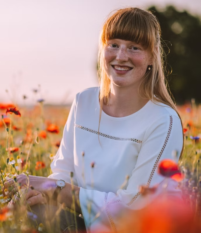 Hannefrone zit glimlachend in een veld met wilde bloemen bij zonsondergang. 
