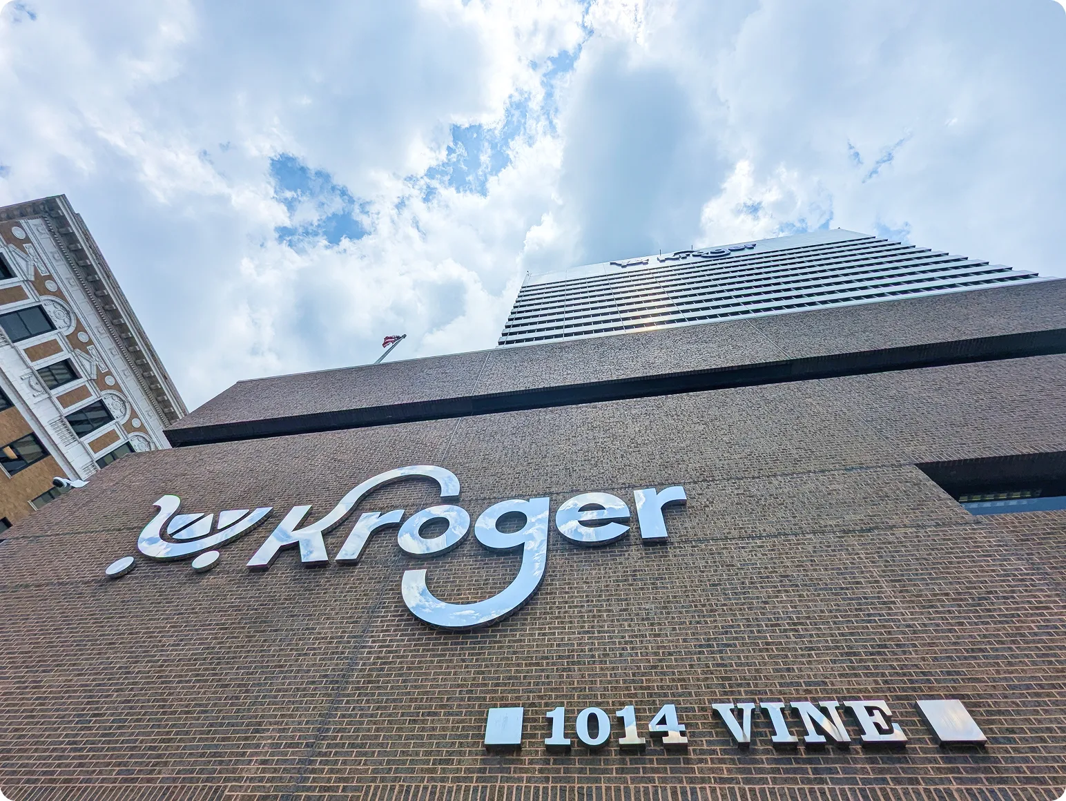 Kroger sign and address 1014 Vine on a brick building with a high-rise and cloudy sky in the background.