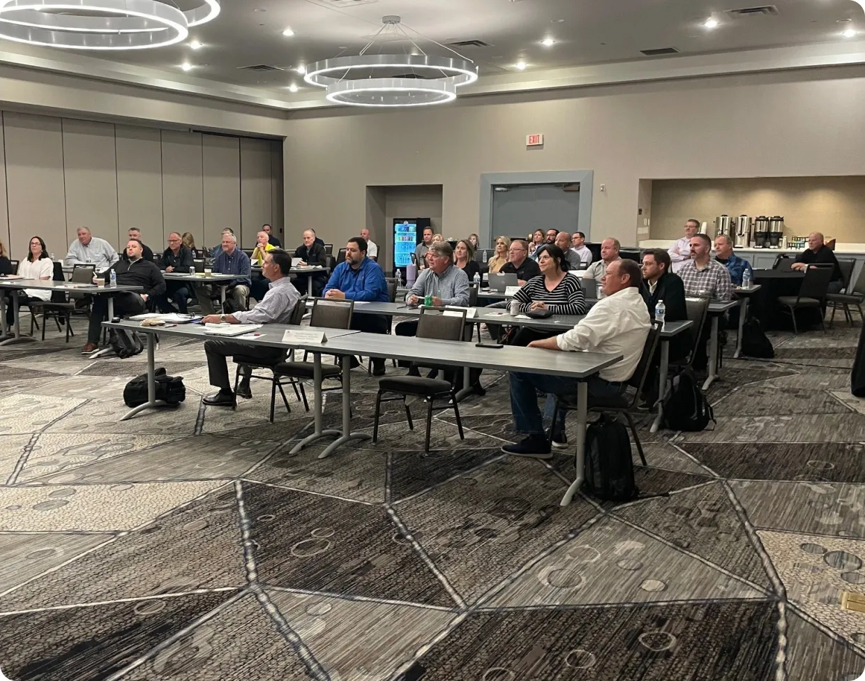 Group of adults seated at tables in a conference room attending a meeting or seminar.