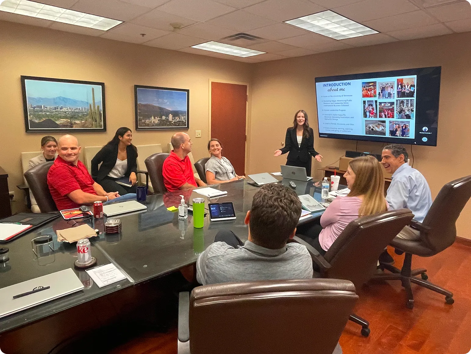 A woman in business attire giving a presentation to a group of people seated around a conference table in an office.