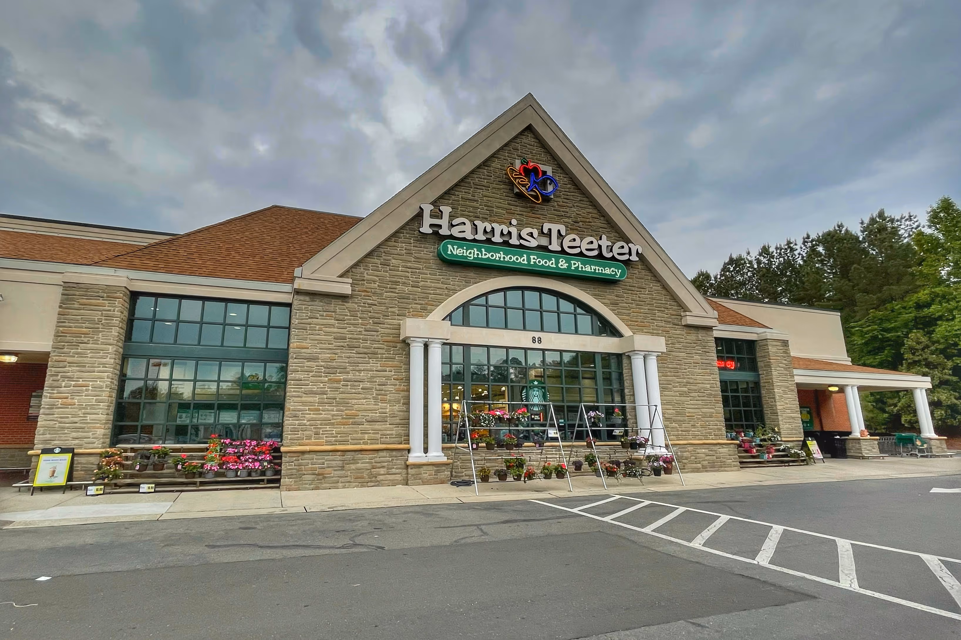 Exterior front view of Harris Teeter grocery store with stone facade, large windows, columns, and flower displays outside.