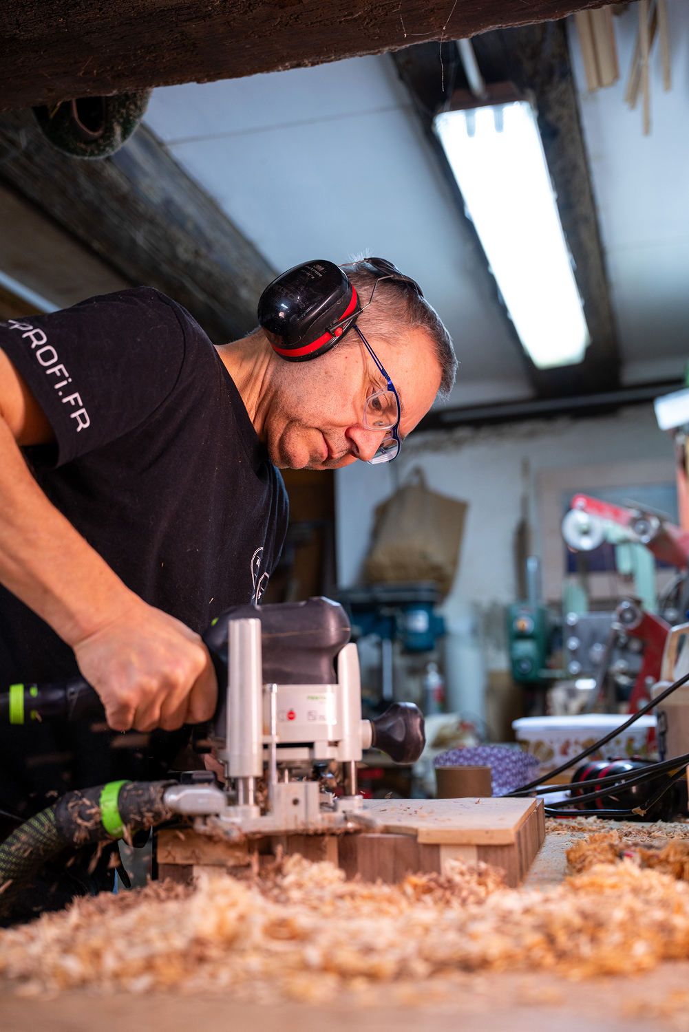 Homme portant des protections auditives et des lunettes de sécurité utilisant une défonceuse électrique pour travailler le bois dans un atelier.