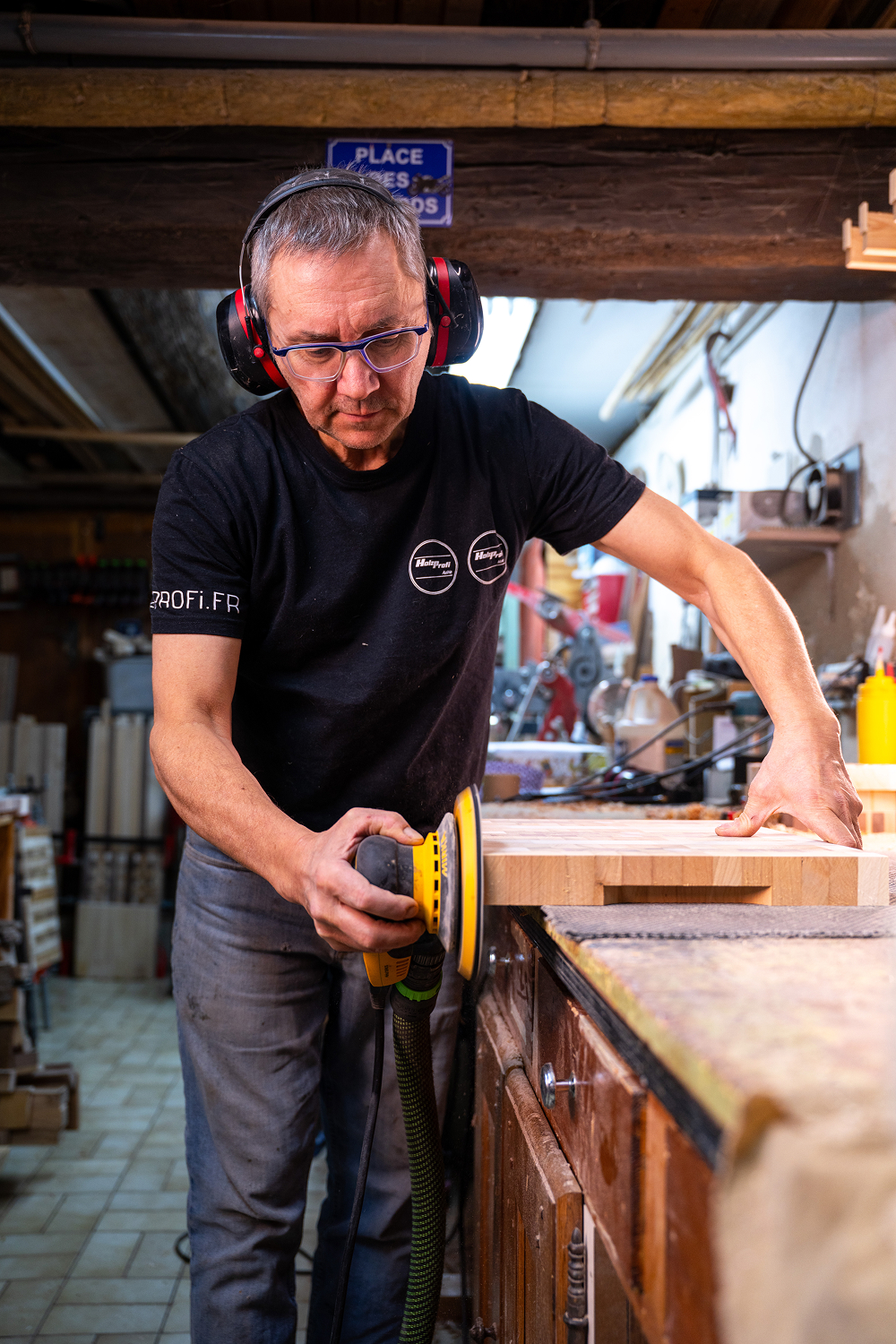 Un homme portant des protections auditives ponce une planche de bois dans un atelier de menuiserie.