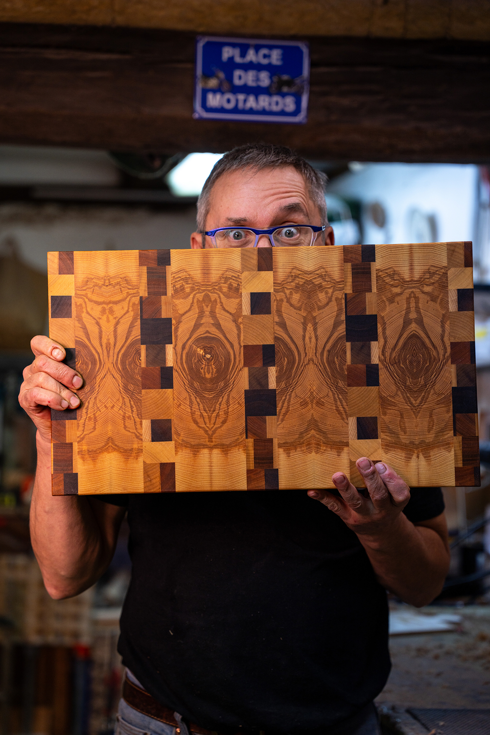 Homme tenant une planche à découper en bois aux motifs symétriques distincts dans un atelier.