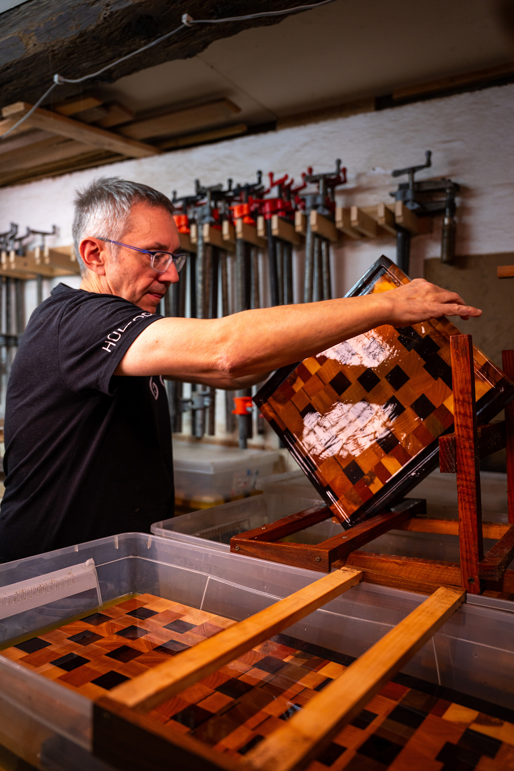Homme inspectant une planche en bois vernissée avec un motif en damier dans un atelier de menuiserie.