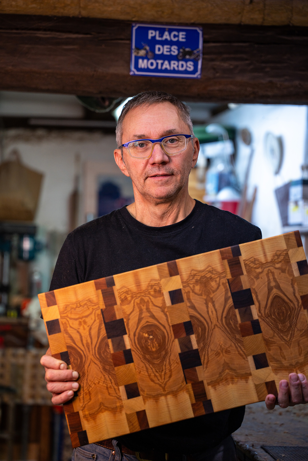Homme portant des lunettes tenant une planche de bois à motifs complexes dans un atelier de bricolage.