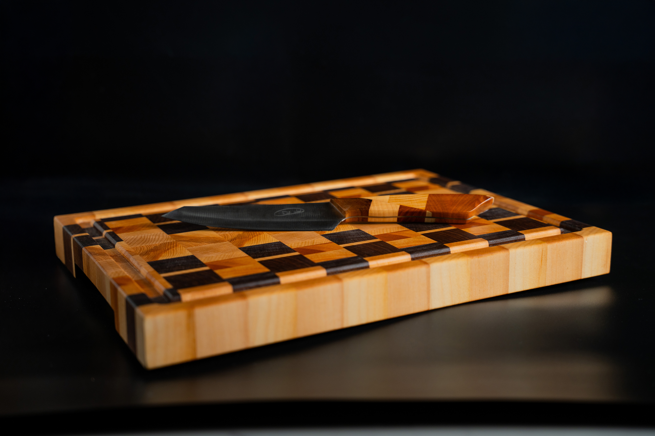 Planche à découper en bois à motifs carrés avec un couteau noir à manche en bois posé dessus.
