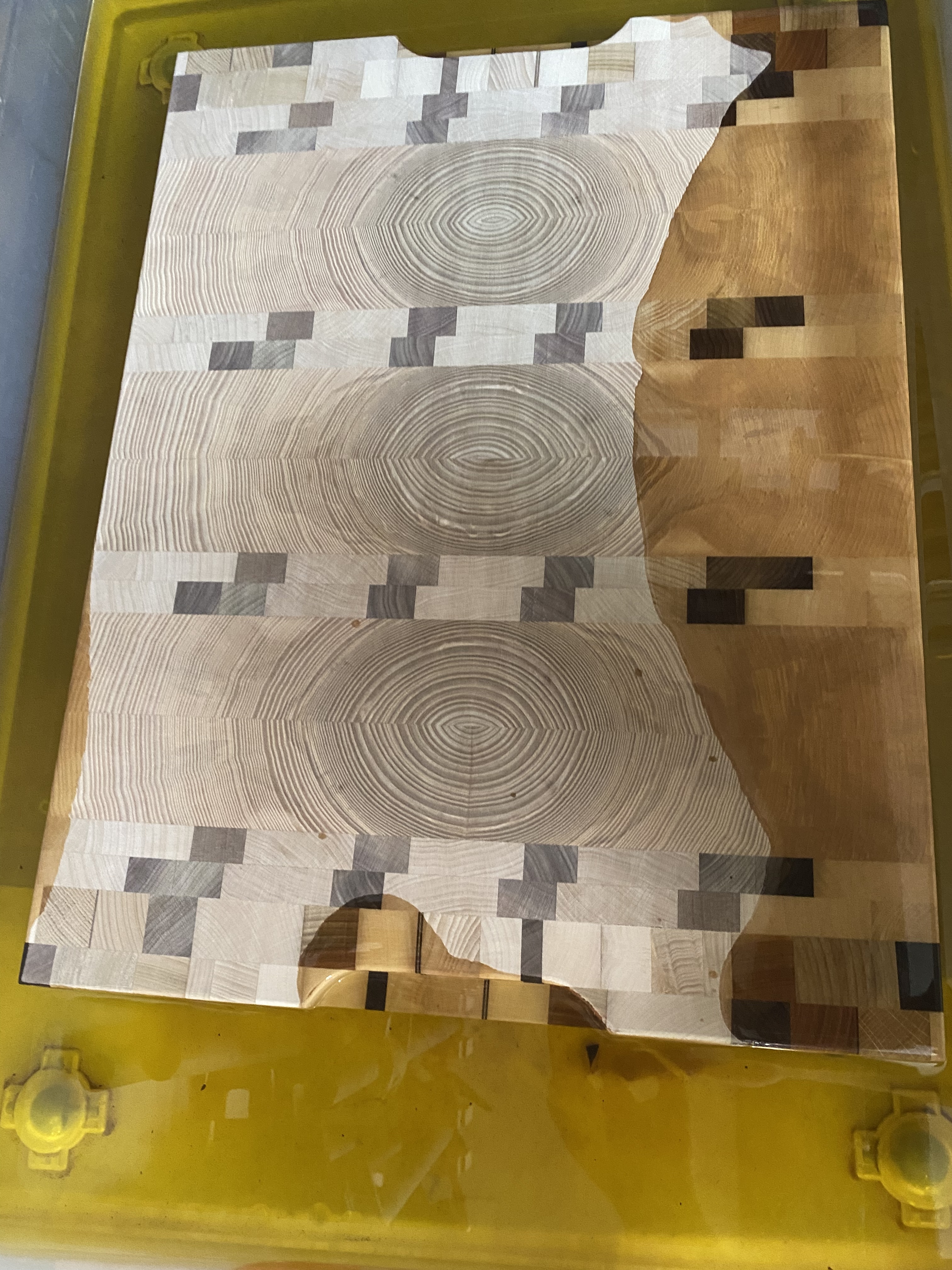 Planche à découper en bois avec motifs de cercles concentriques et carrés, posée sur une surface jaune.