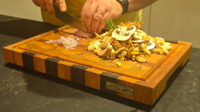 Une personne coupe des légumes et champignons frais sur une planche à découper en bois.