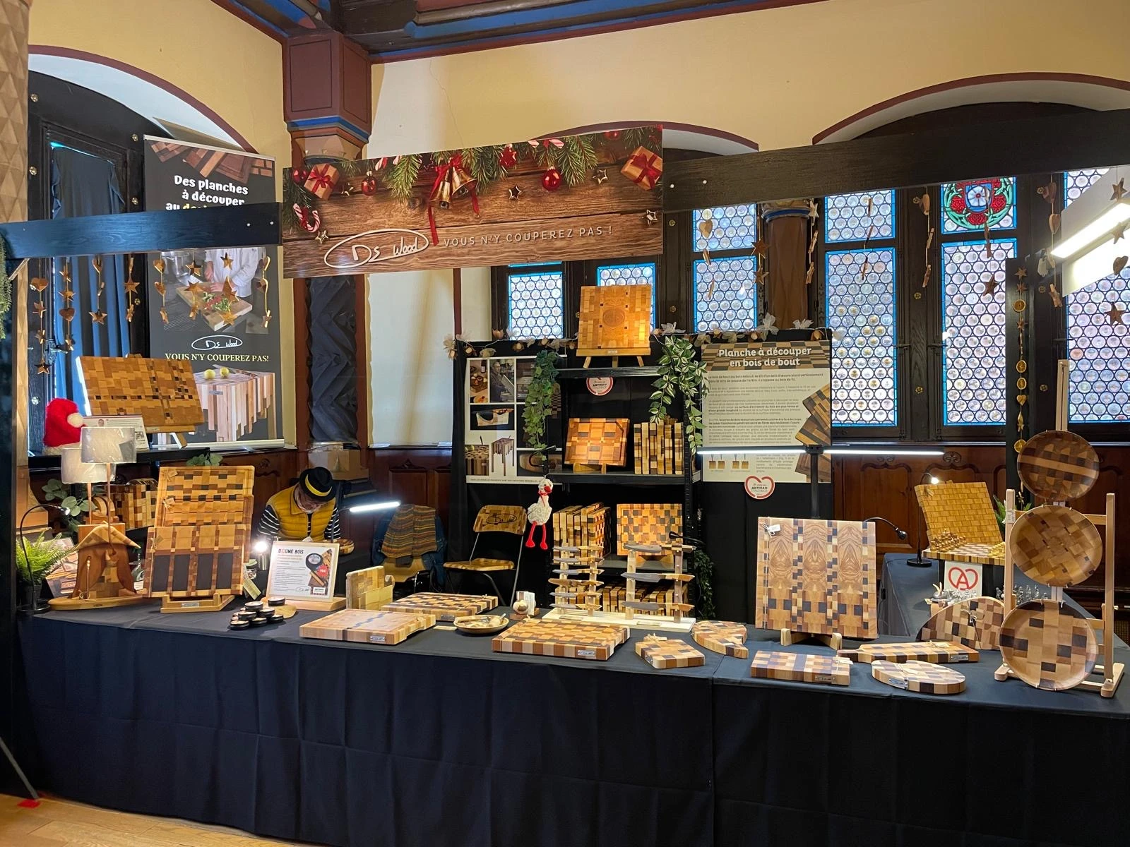 Stand d'exposition présentant diverses planches à découper en bois avec motifs variés dans une salle avec fenêtres à vitraux.