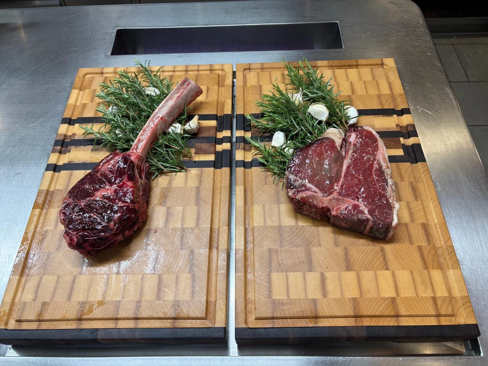 Deux planches en bois avec une pièce de viande crue garnie de brins de romarin et de gousses d'ail sur chacune.