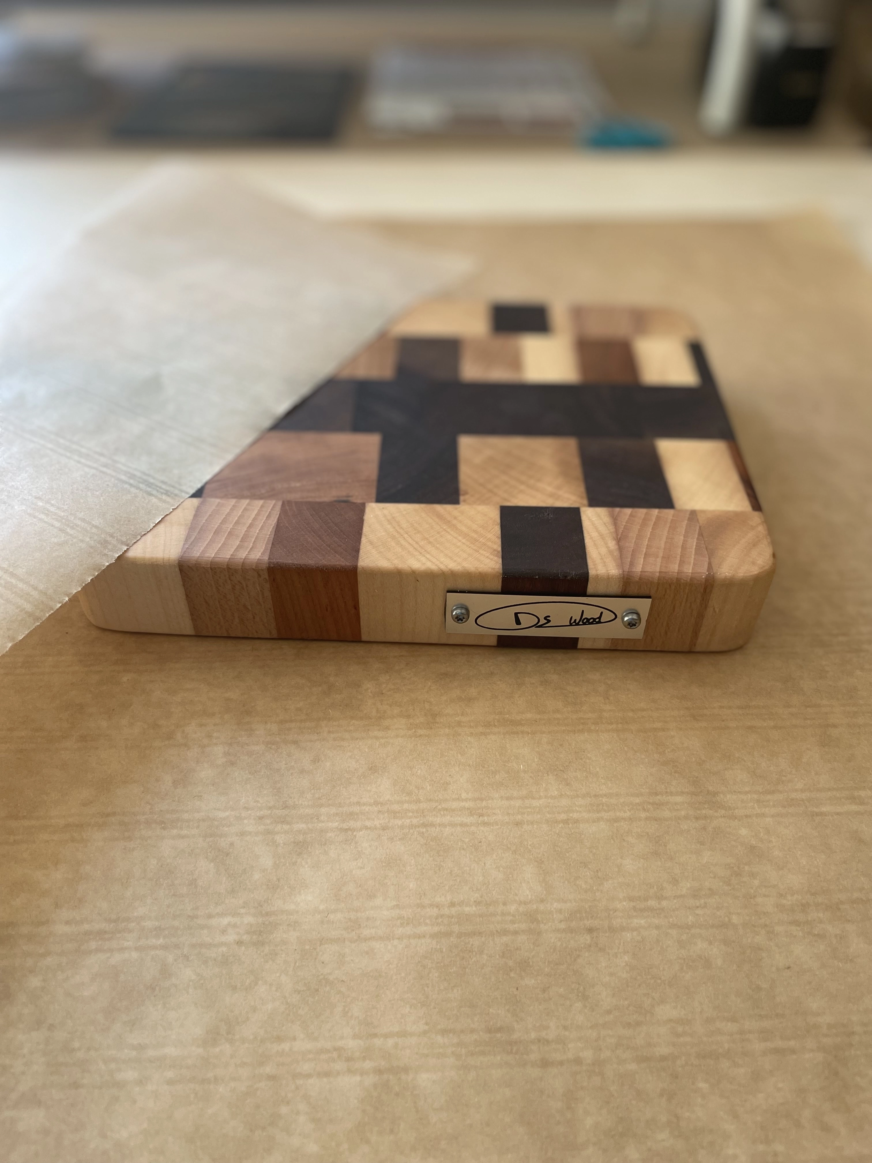 Planche à découper en bois en damier avec plaque métallique gravée posée sur une surface en papier brun.