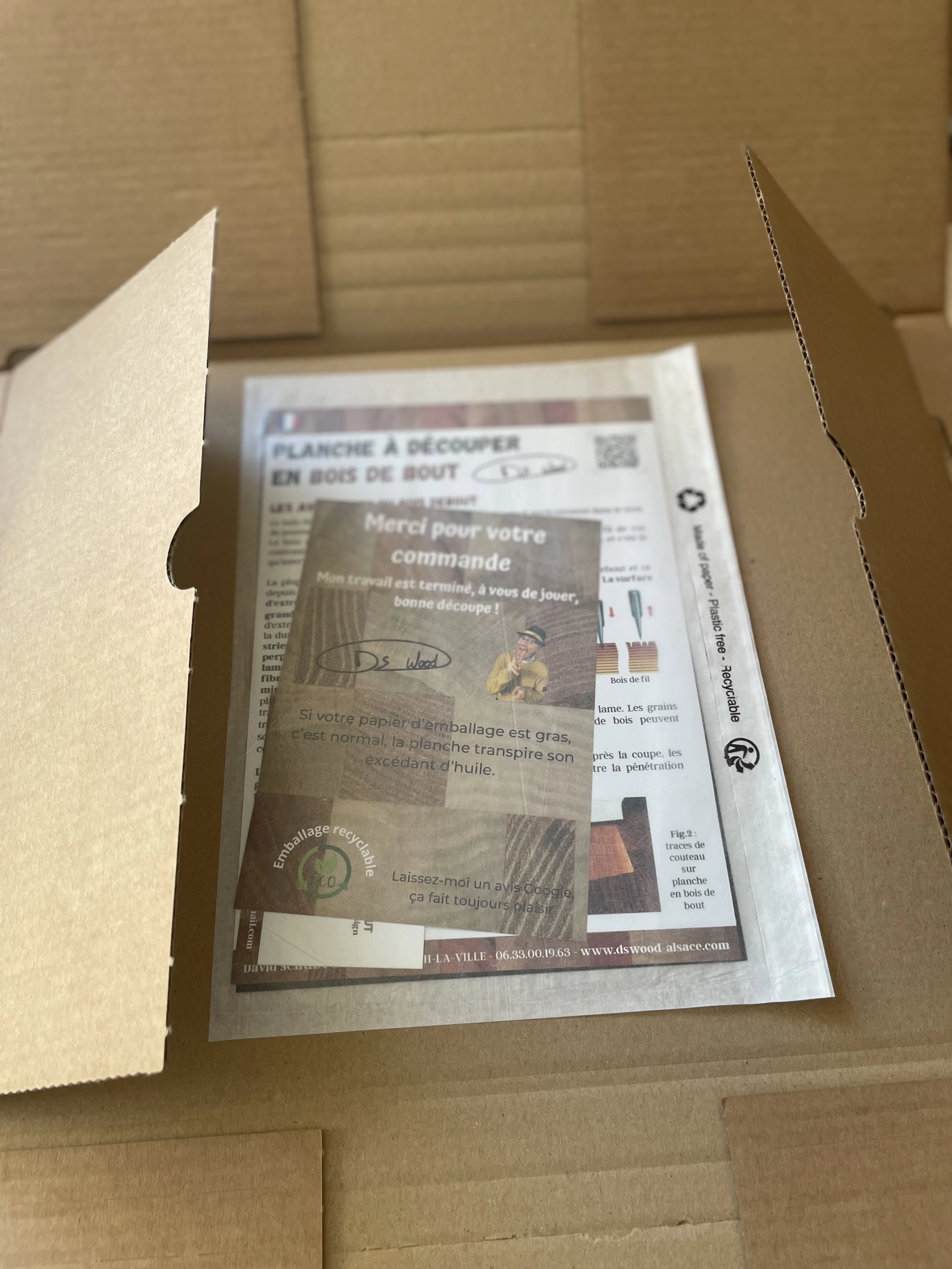 Carte de remerciement et instructions sur une planche à découper en bois de bout dans un emballage en carton recyclable.