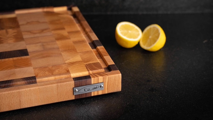 Planche à découper en bois clair et foncé sur un plan de travail noir avec deux moitiés de citron jaune à côté.