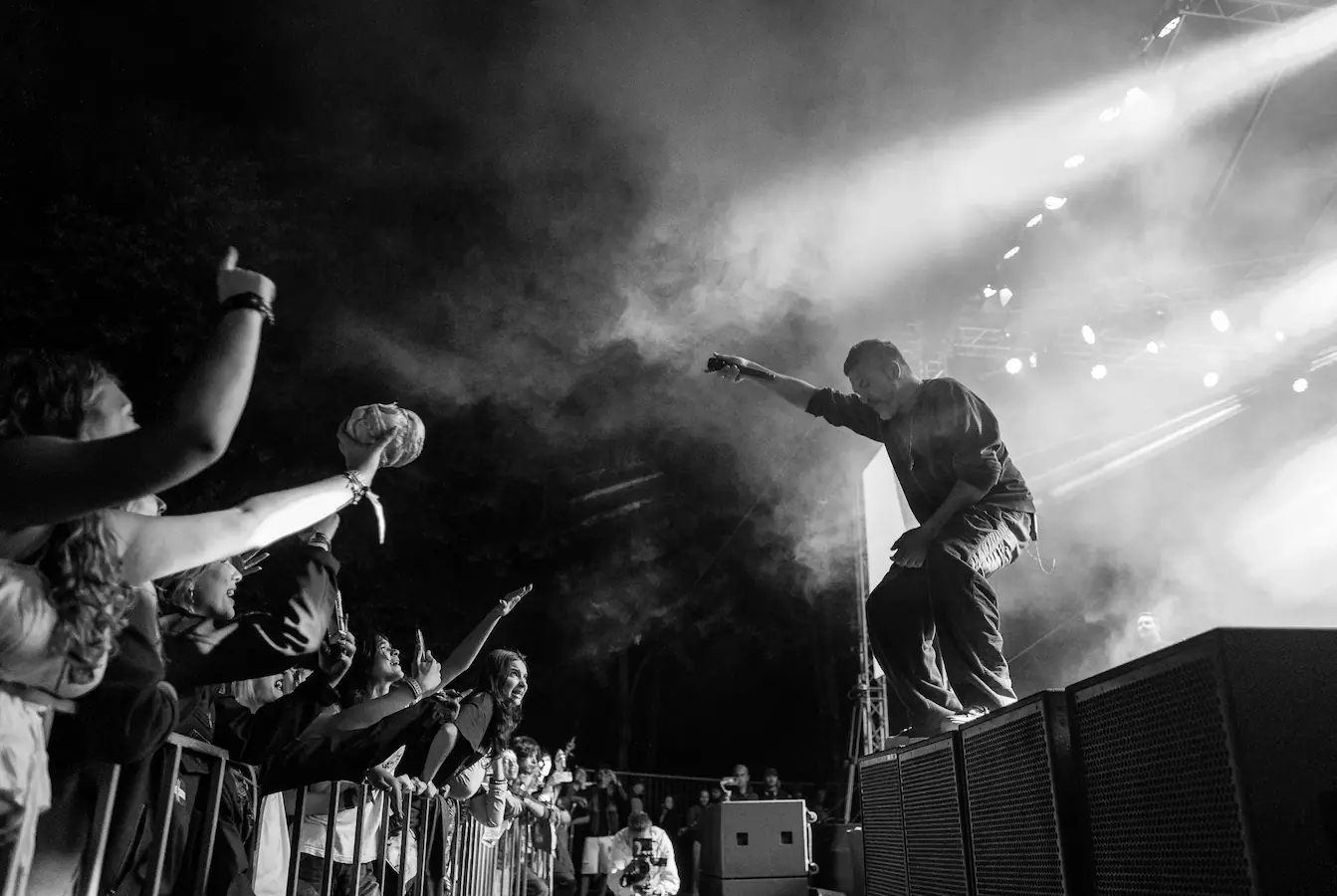 Black and white photo of a musician performing on stage with crowd reaching towards him at a concert.