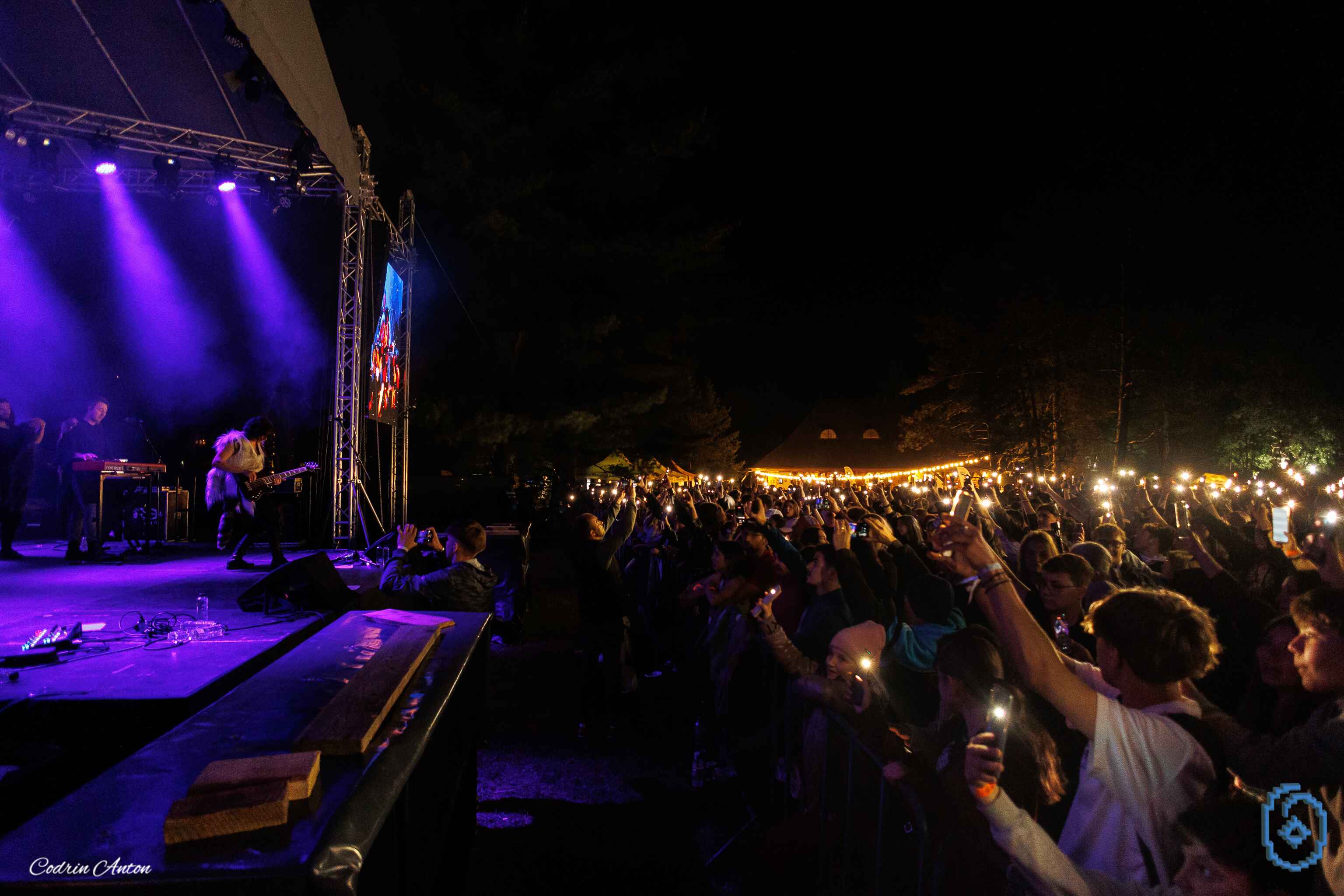 Concert rock nocturn cu o trupă pe scenă și mulțime de spectatori ținând telefoanele aprinse.