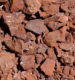 Close-up view of rough reddish-brown iron ore rocks piled together, showing uneven textures and natural mineral surfaces in sunlight.