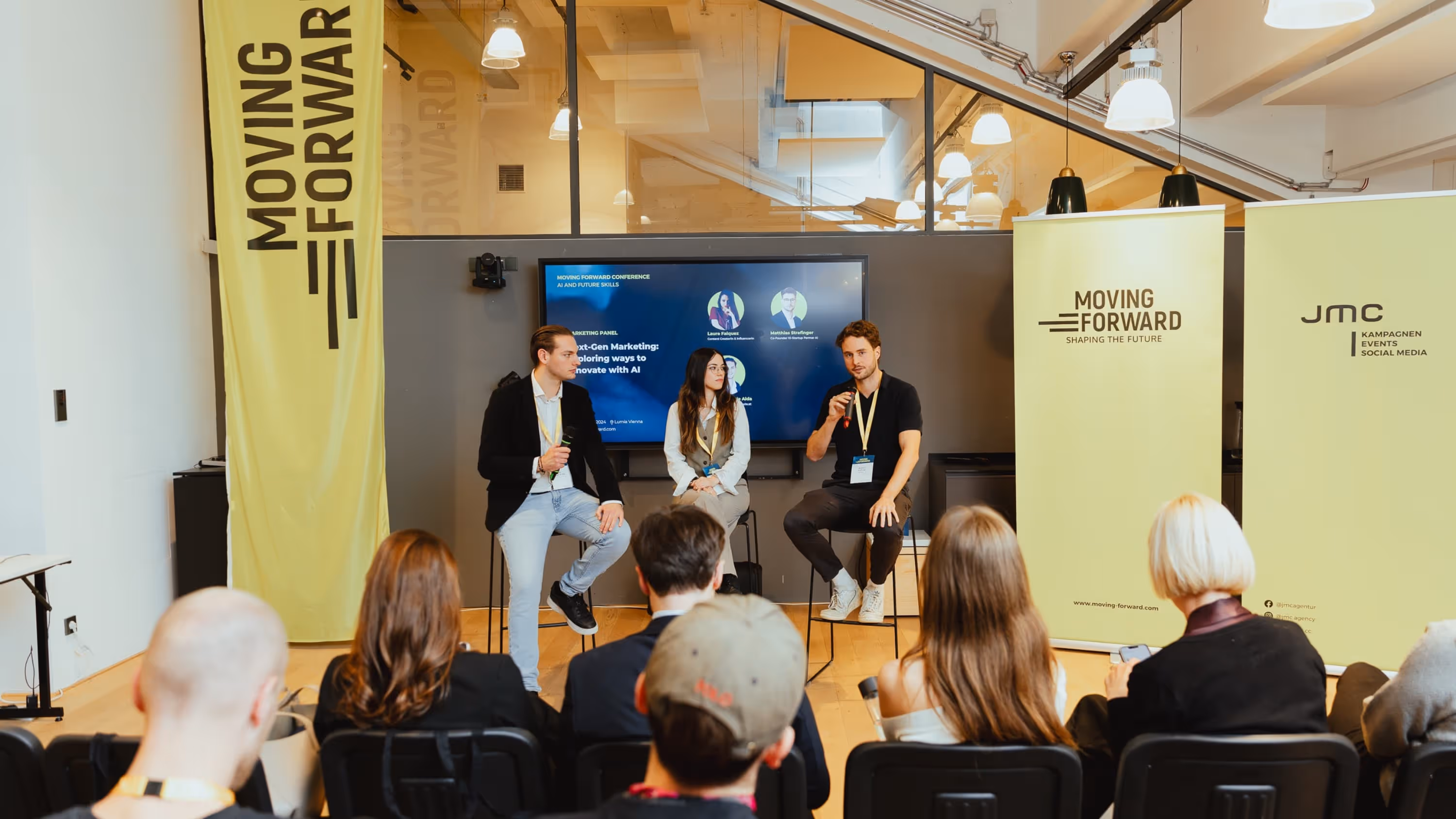 Three panelists seated on stools speaking to an audience at a Moving Forward conference about next-gen marketing and AI.