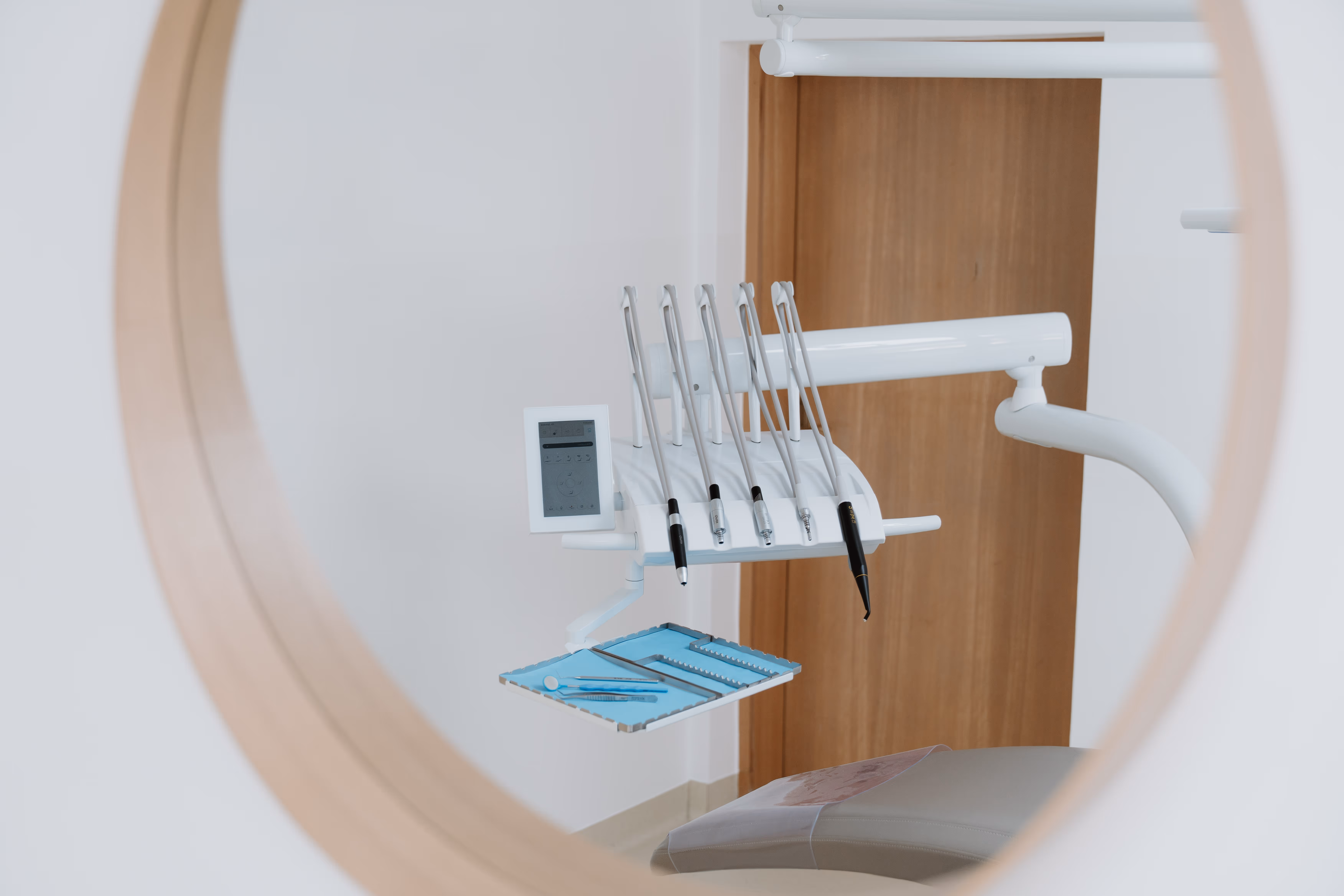 Zahnarztinstrumente und Mundspiegel auf einem Tablett neben einem Behandlungsstuhl, reflektiert in einem runden Spiegel.