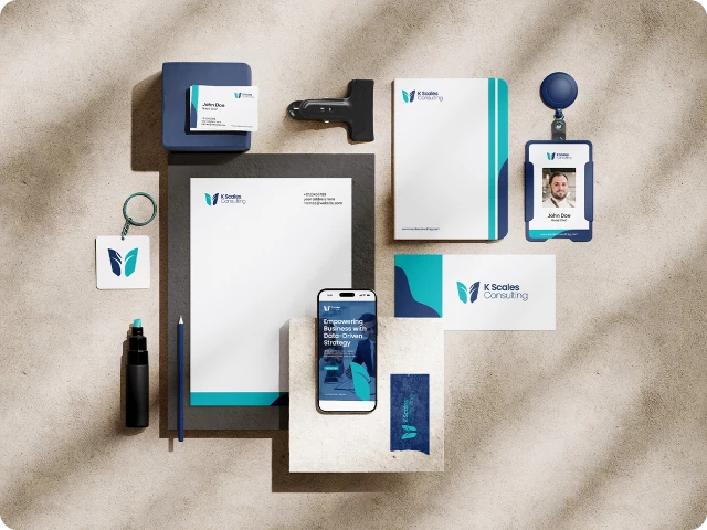 Flat lay of K Scales Consulting branded stationery including letterhead, business card, ID badge, notebook, pen, phone displaying company website, stamp, and keychain, arranged on a textured surface with natural light.