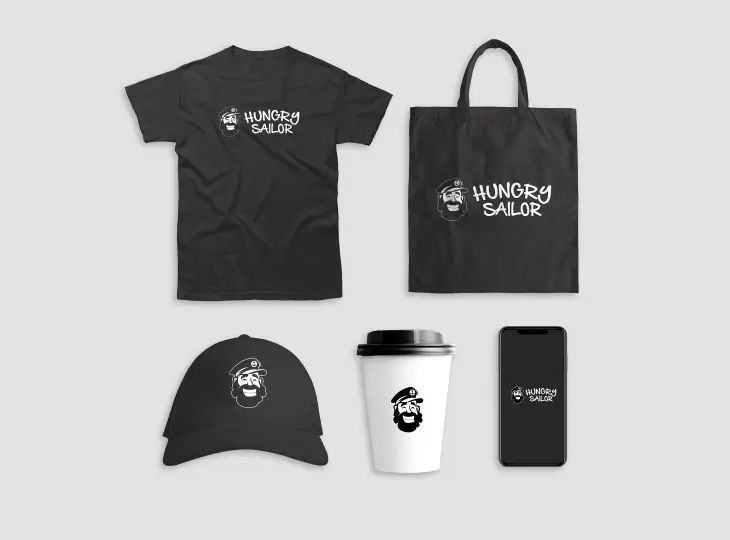 Set of Hungry Sailor branded items including a black t-shirt and tote bag with logo text and sailor icon, black cap with sailor icon, white coffee cup with black lid and sailor icon, and smartphone displaying logo on screen.