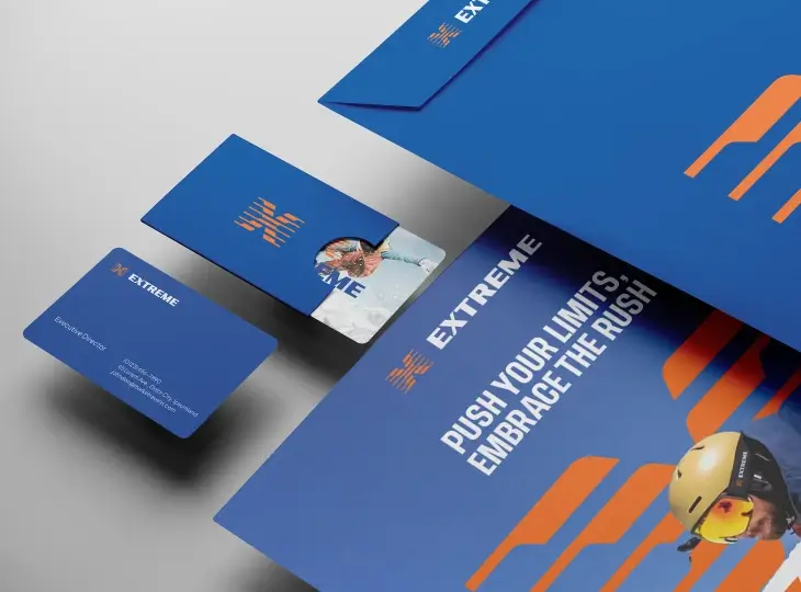 Blue branded stationery including business cards, envelope, and folder with orange logo and slogan 'PUSH YOUR LIMITS, EMBRACE THE RUSH' featuring a skier wearing a helmet and goggles.
