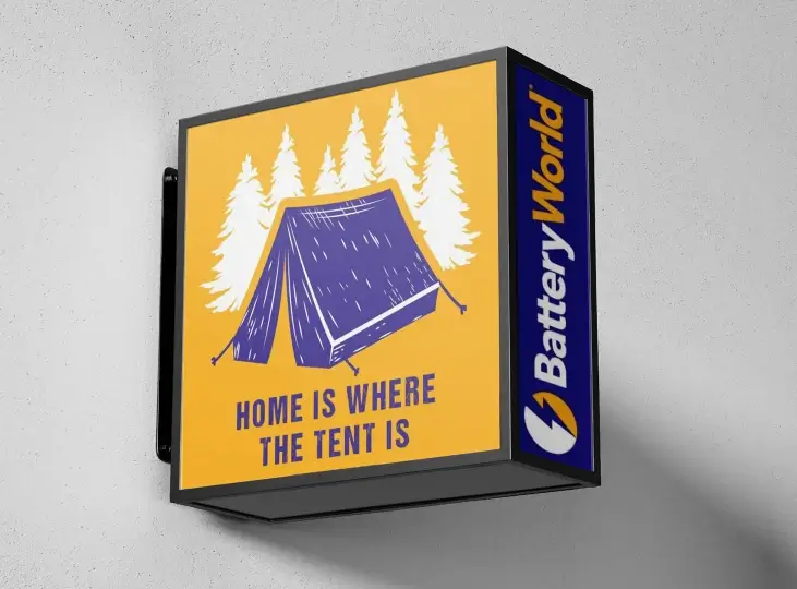 Outdoor sign with illustration of a purple tent and white pine trees, text reads 'Home is where the tent is' and side panel shows Battery World logo.