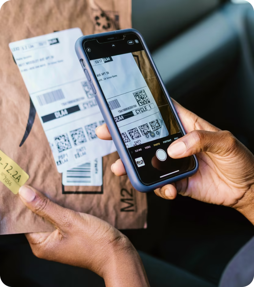 Person using smartphone camera to scan barcode on a brown package with shipping labels.